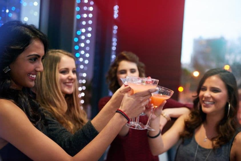Garotas brindando com bebidas em um bar de coquetéis.