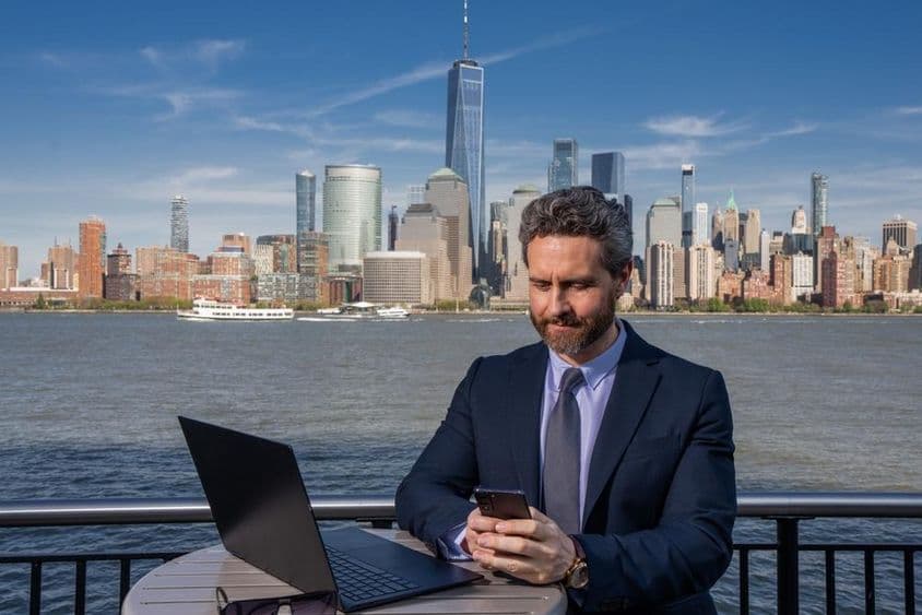 Empresário usando laptop ao ar livre, trabalhando remotamente.