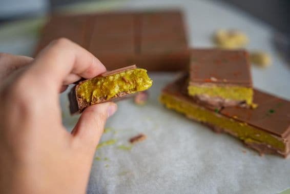 Pedaço de chocolate de Dubai com pistache e massa kataifi na mão de uma mulher.