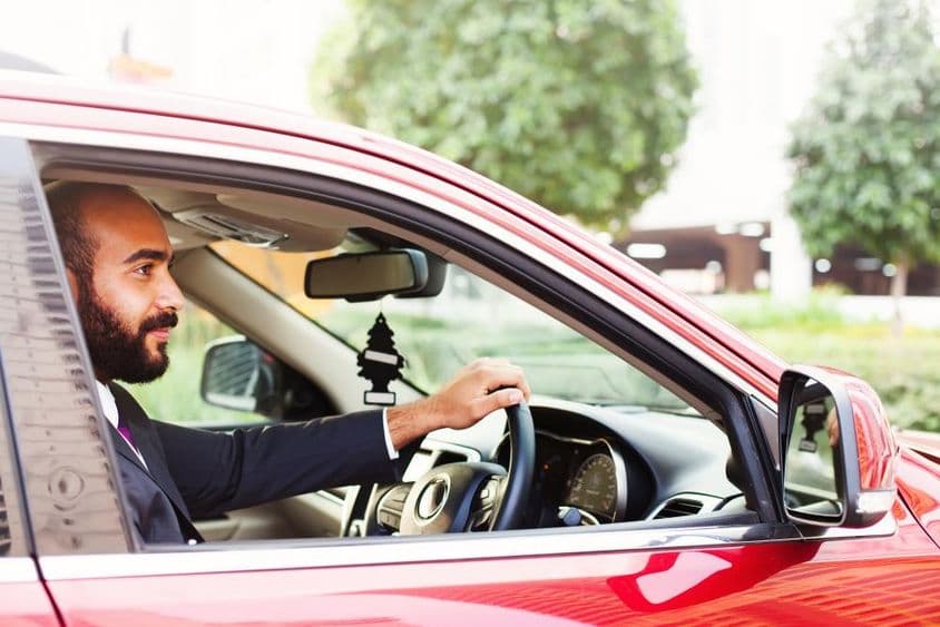 Jovem empresário dirigindo um carro alugado vermelho.