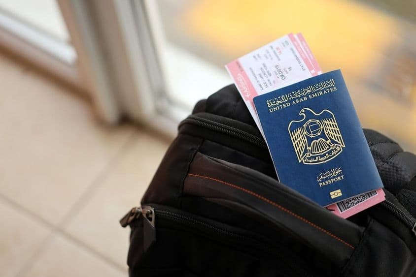 Passaporte azul dos Emirados Árabes Unidos com passagens aéreas em uma mochila de perto.