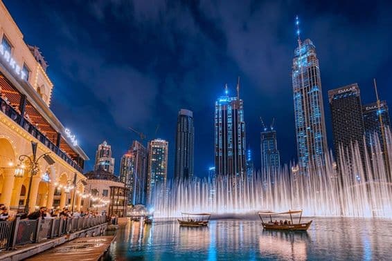 Pessoas navegando enquanto assistem ao show da fonte de Dubai à noite, com arranha-céus de Dubai ao fundo.