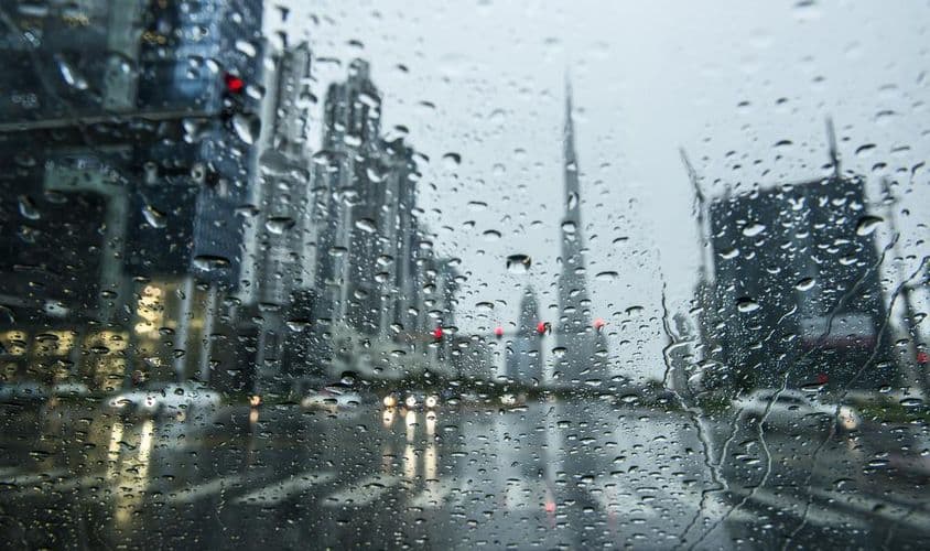 Chuva em Dubai, vista desfocada através de uma janela chuvosa, silhuetas do Burj Khalifa ao fundo.