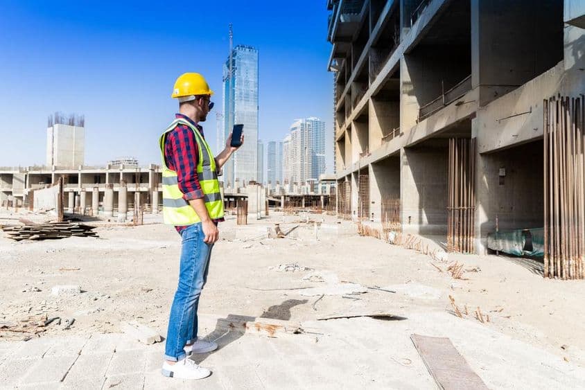 Homem usando smartphone em canteiro de obras em Dubai com horizonte da cidade ao fundo.