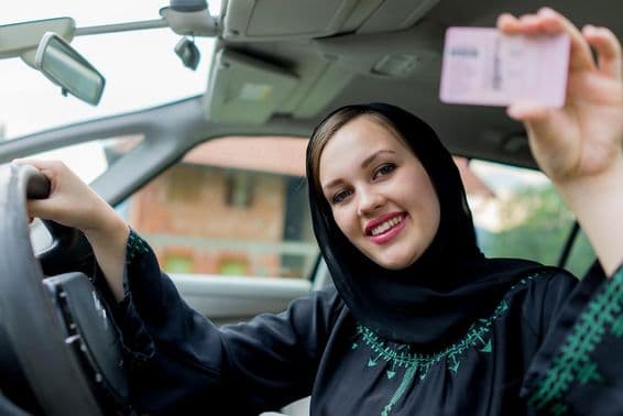 Mulher muçulmana dirigindo um carro, segurando uma carteira de motorista.