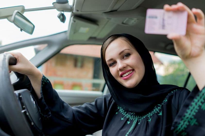 Mulher muçulmana dirigindo um carro, segurando uma carteira de motorista.