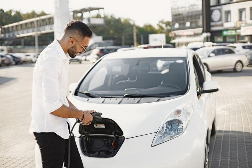 Jovem árabe carregando um carro elétrico branco.