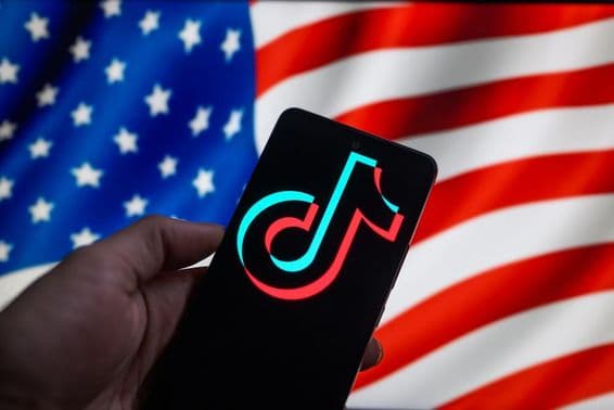 O logotipo do TikTok exibido em um smartphone com a bandeira dos EUA ao fundo.