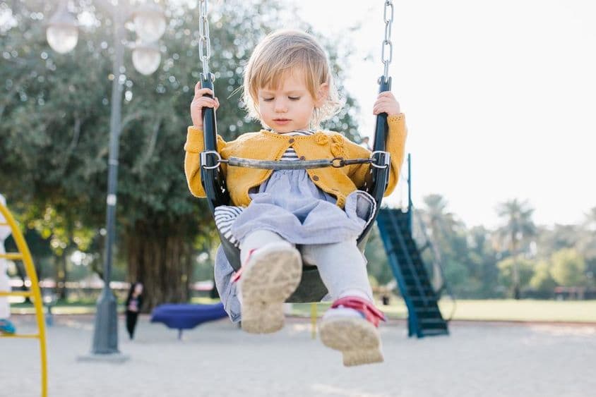 Menina pequena alegre balançando no parque sob o sol.