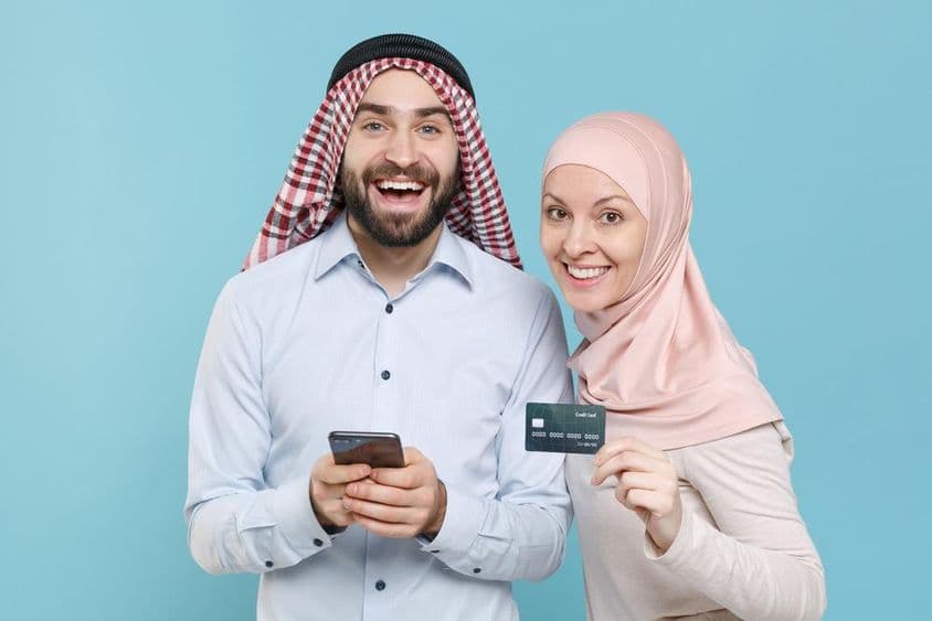 Casal sorridente segurando cartão de crédito e telefone.