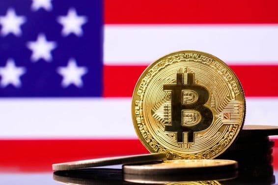 Moeda de metal Bitcoin dourada com a bandeira dos EUA ao fundo.