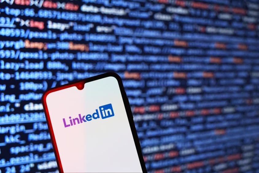 Smartphone exibindo logotipo do LinkedIn com trecho de código ao fundo.