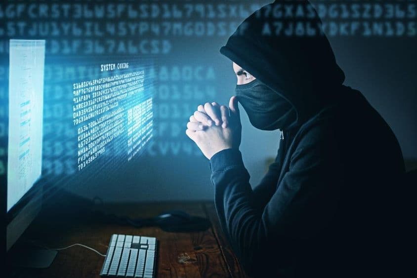 Cibercrime, homem encapuzado sentado em frente a um computador.