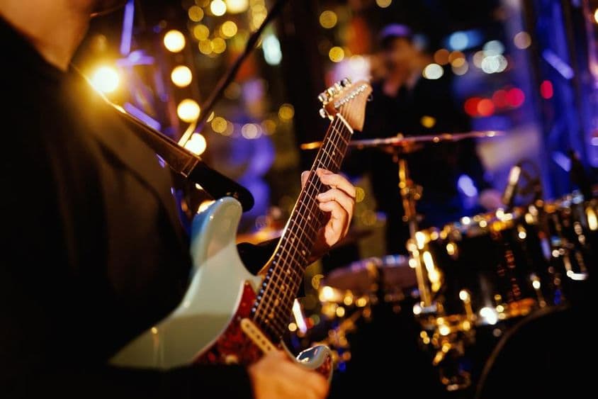 Um guitarrista tocando um acorde no braço da guitarra durante a apresentação de uma banda.