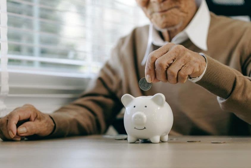 Economizando dinheiro, idoso colocando moedas em um cofrinho