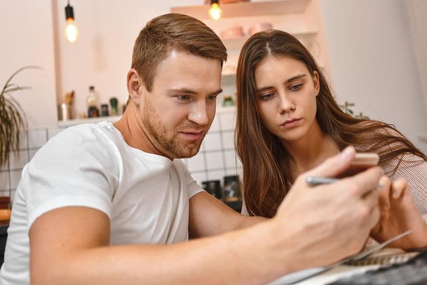 Casal jovem desfrutando de café na cozinha enquanto lê uma notificação bancária online no celular.