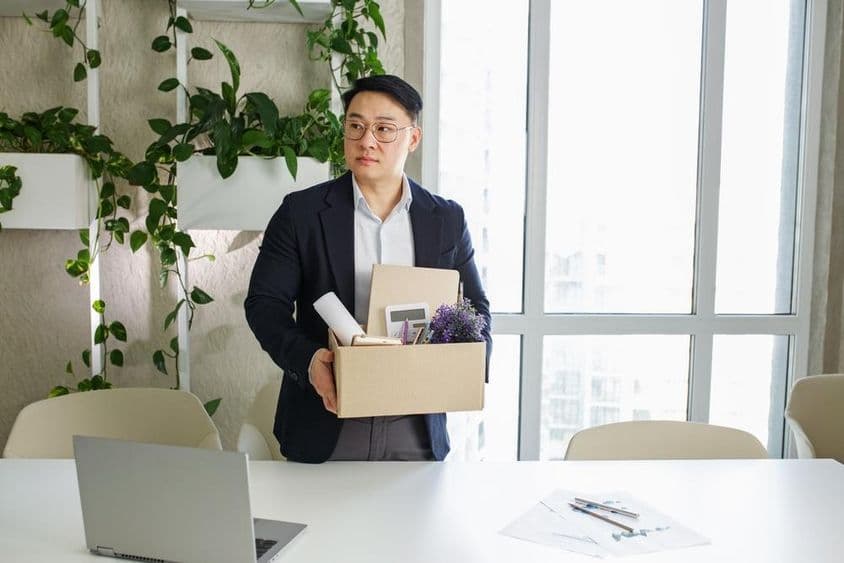 Um homem sendo demitido de seu local de trabalho, colocando seus pertences pessoais em uma caixa de papelão.
