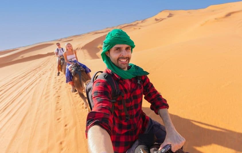 Uma pessoa desfrutando de um passeio em grupo enquanto monta um camelo no deserto.
