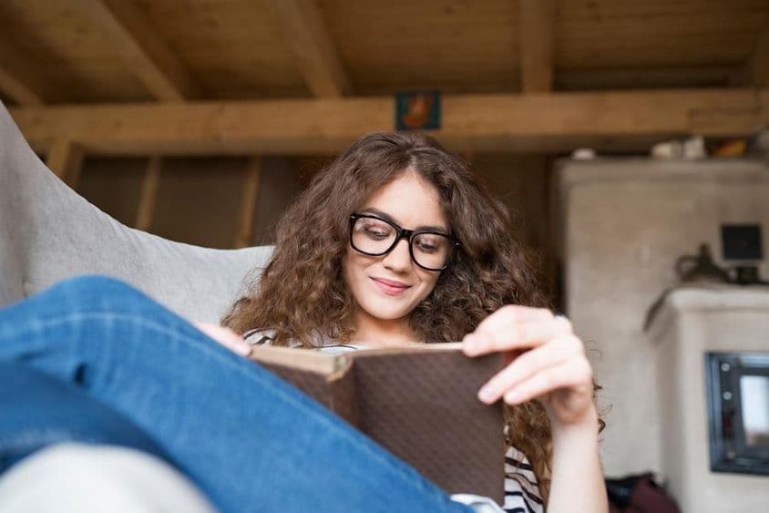 Estudante sentada em uma poltrona lendo um livro.