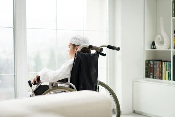 Um jovem em cadeira de rodas olhando pela janela.