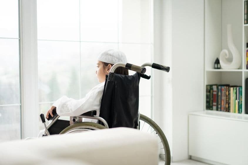 Um jovem em cadeira de rodas olhando pela janela.