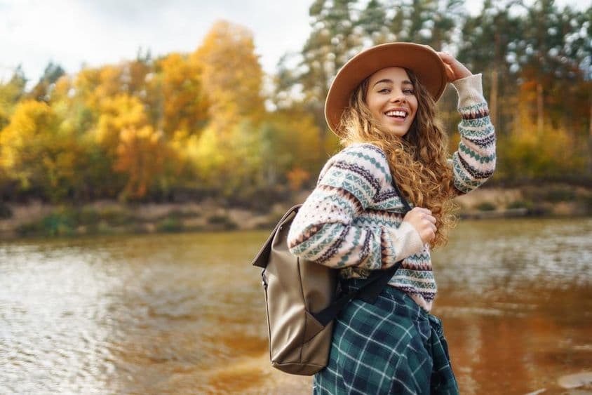 Viajante feminina com mochila e boné apreciando uma caminhada de outono ao longo de um rio.