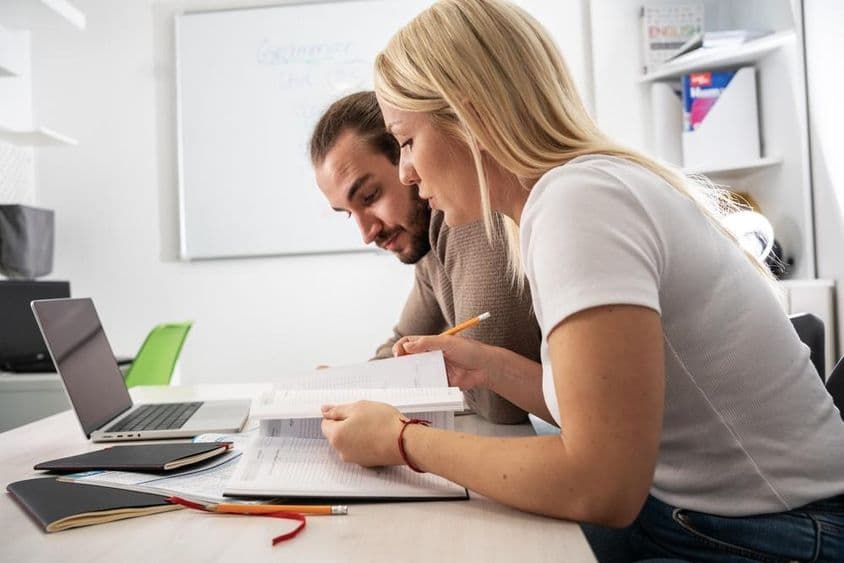 Dois estudantes lendo material de curso em um caderno.