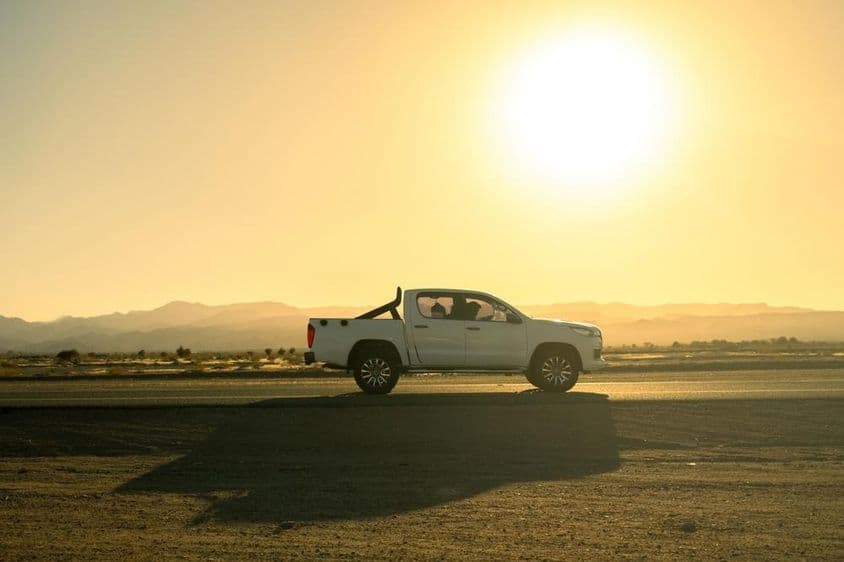 Veículo pickup branco em viagem pelo campo, dia ensolarado ao pôr do sol.