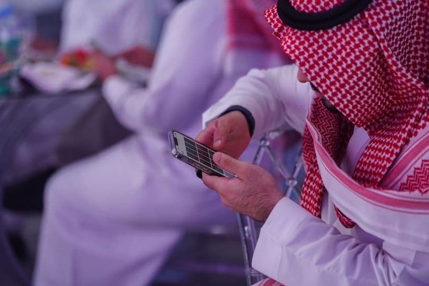 Homem árabe trabalhando no celular, lendo ou digitando uma mensagem.