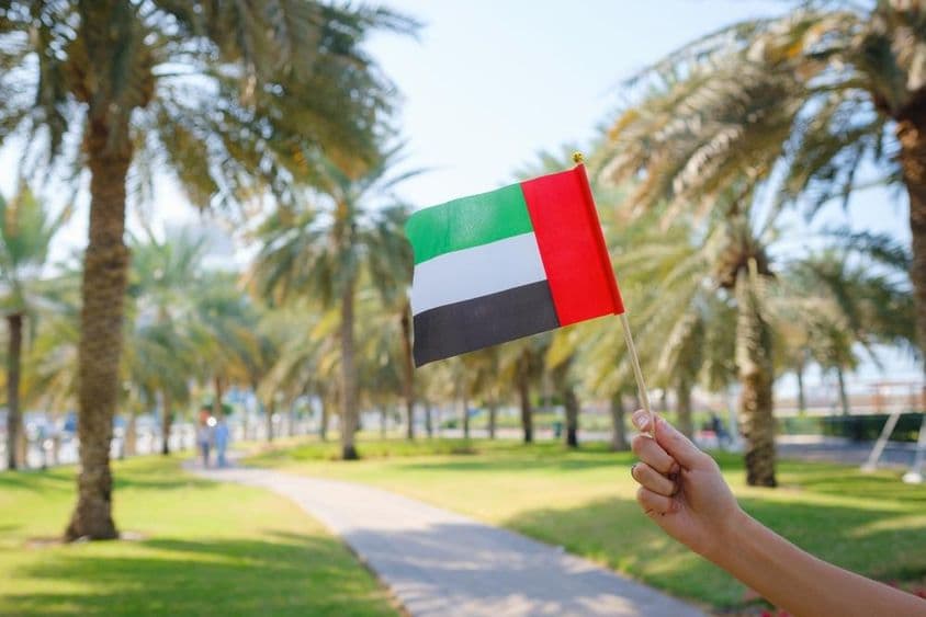 A mão de uma mulher segurando uma miniatura da bandeira dos Emirados Árabes Unidos em um parque de Abu Dhabi.