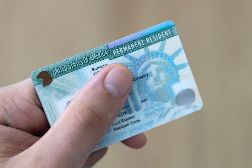 Um residente permanente nos EUA segura um green card na mão.