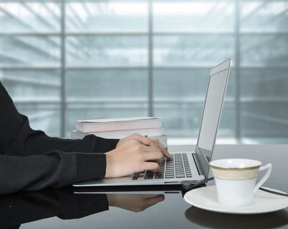Uma mulher trabalhando em um laptop com uma xícara de café ao lado.