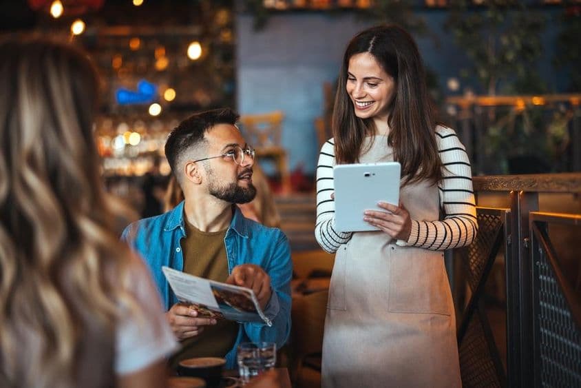 Uma garçonete sorridente recebe um pedido em um bar aconchegante.