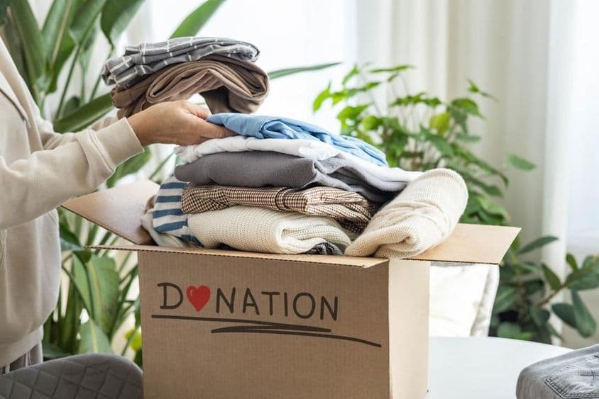 Uma mulher em casa colocando roupas em uma caixa de papelão para doação, para reciclagem.
