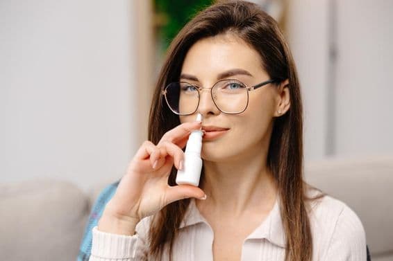 Jovem mulher usando um spray nasal para facilitar a respiração.