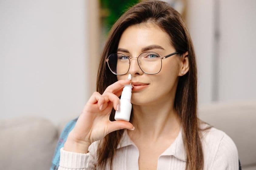 Jovem mulher usando um spray nasal para facilitar a respiração.