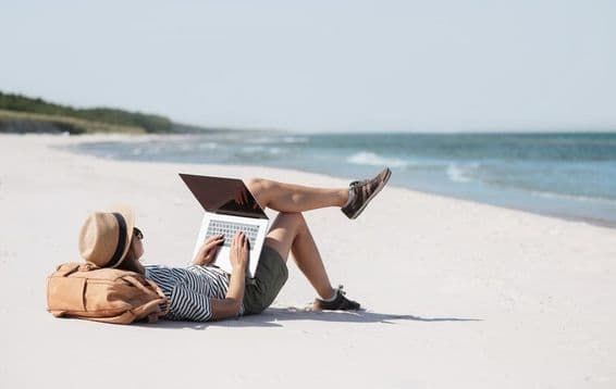 Mulher jovem trabalhando em um laptop à beira-mar fazendo trabalho freelance.