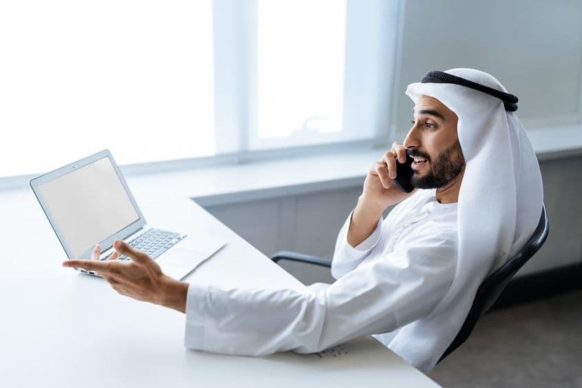 Um empresário bem-sucedido com traje tradicional Emirati branco trabalhando em Dubai.