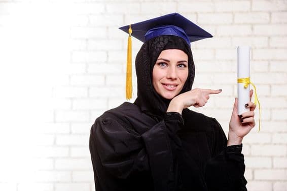 Formanda muçulmana feliz posando com diploma em ambiente interno.