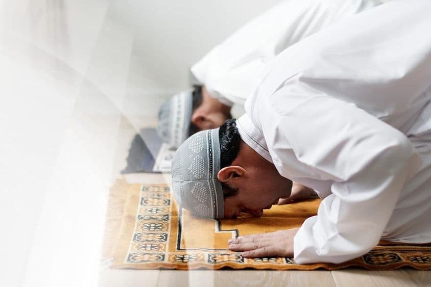 Homens islâmicos vestidos de branco inclinados em oração.