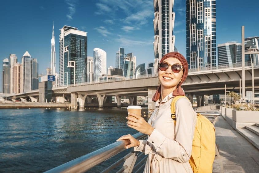 Mulher muçulmana com uma mochila amarela caminhando pelo canal de Dubai.