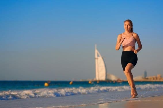 Jovem mulher correndo na praia em Dubai com o Burj Al Arab Jumeirah ao fundo.