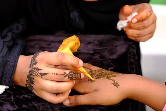 Uma garota aplicando design de henna na mão de outra.