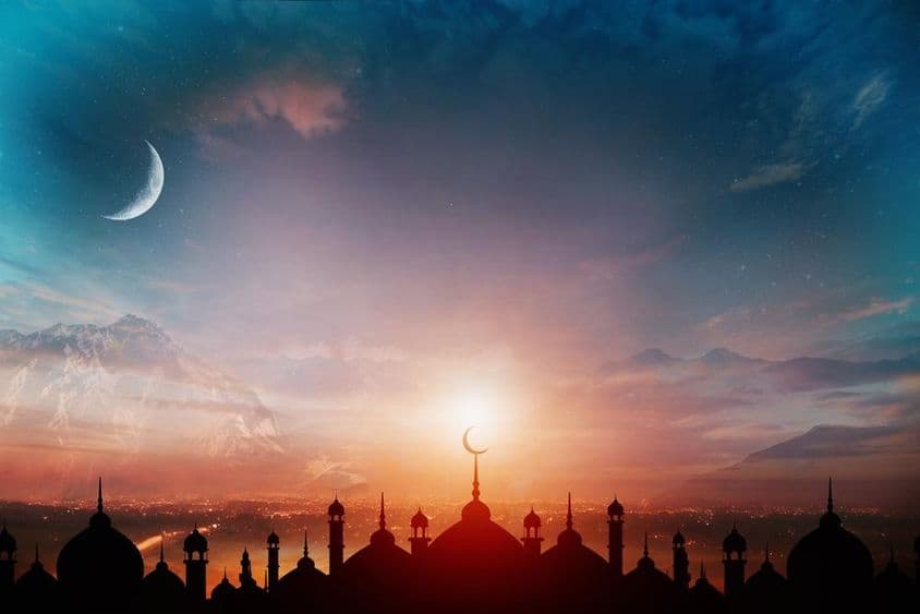 Domos de mesquita contra um céu azul crepuscular com uma lua crescente ao fundo.