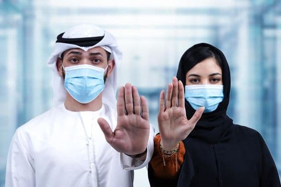 Homem e mulher árabes com máscaras médicas fazendo gesto de parada.