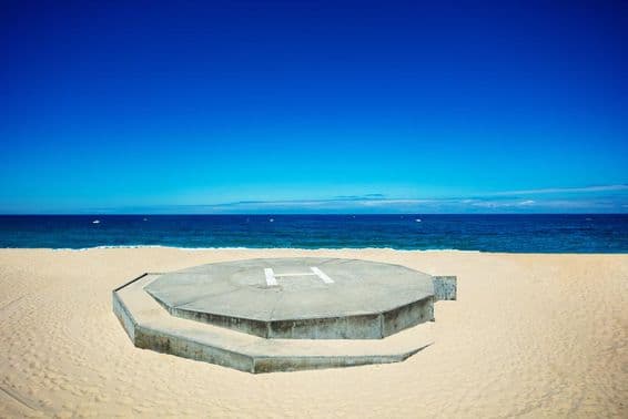 Helicóptero pousando em uma praia de areia próxima a um oceano azul.