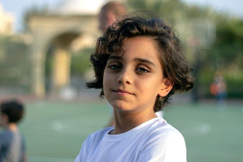 Um menininho fofo em pé em uma quadra de basquete e sorrindo.