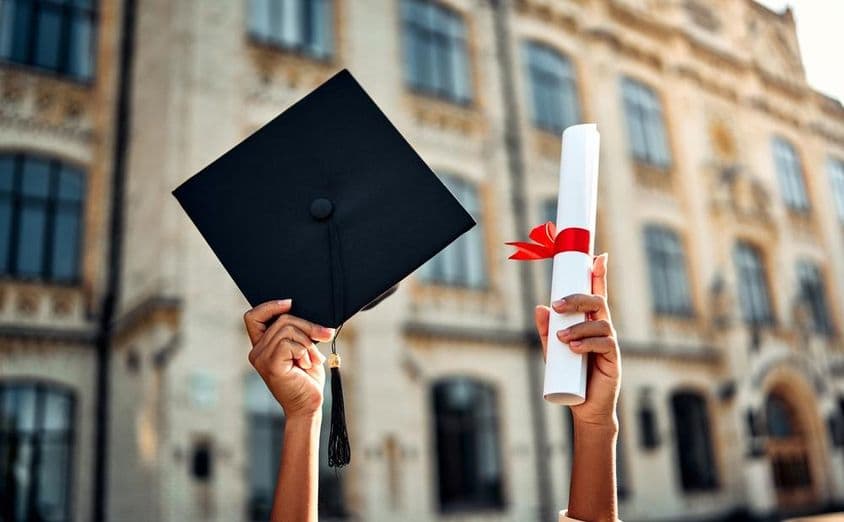Capelo de formatura e diploma com laço vermelho.