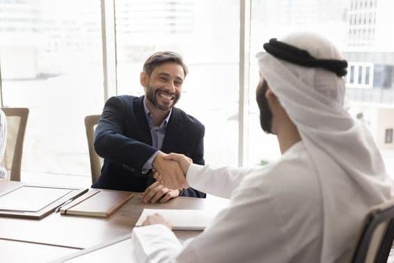 Empresário sorridente apertando as mãos com parceiro árabe.