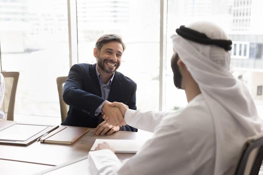 Empresário sorridente apertando as mãos com parceiro árabe.